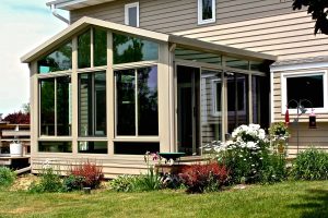Outer view of a sunroom and some green area with flowers near it.