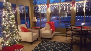 Picture of the interior of a sunroom with a Christmas tree and holiday string lights, with a snow-covered backyard in the background.